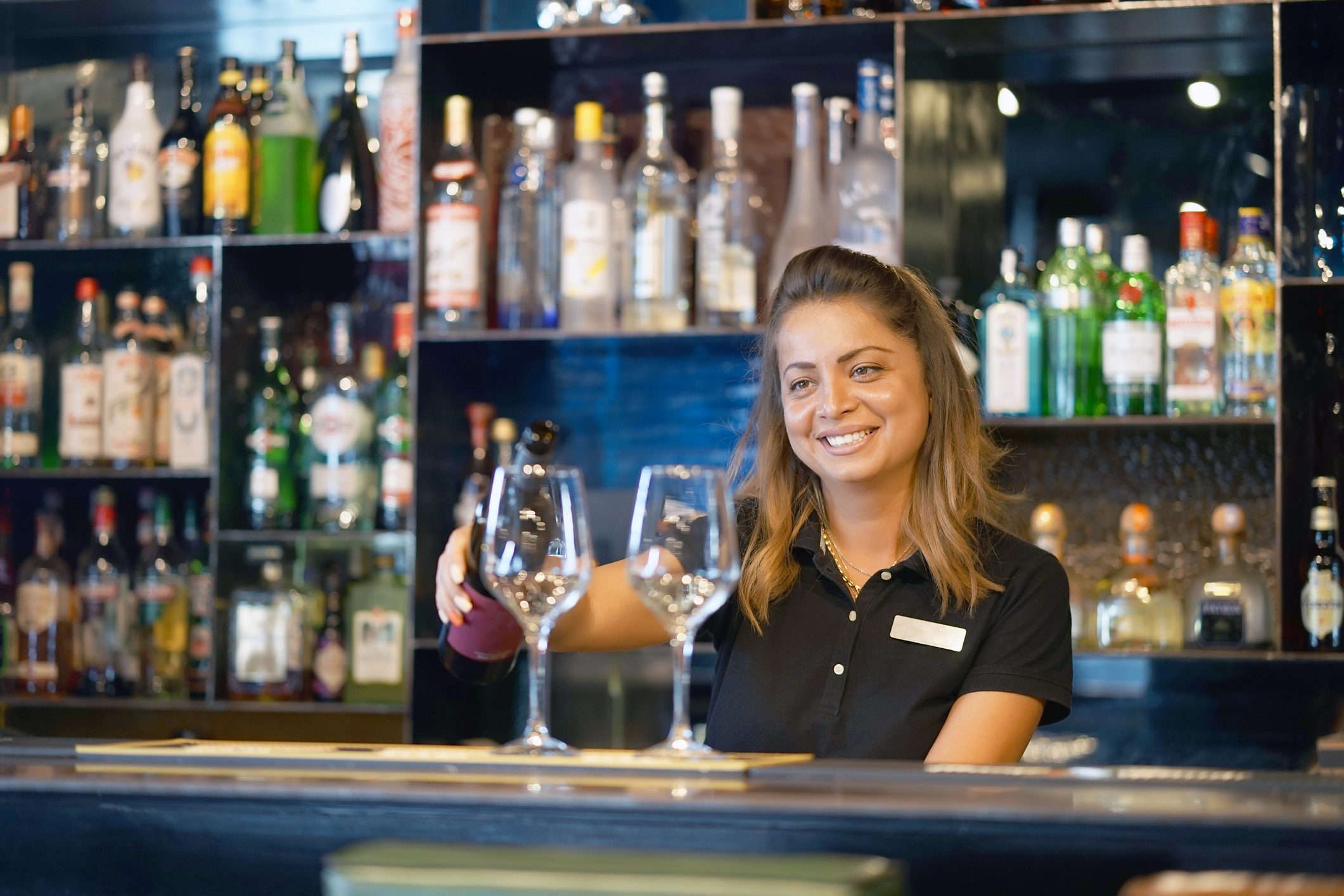 Smiling girl bartender pours wine into a wine glass
